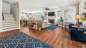 A spacious living room with a fireplace, a dining area, and a kitchen in the background. - Luxury 2nd Row Home, Chefs Kitchen, Pool, Free Golf, Great for Entertaining (Hilton Head)