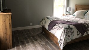 A bedroom with a wooden bed, a nightstand with a lamp, a window with blinds, and a TV on a wooden stand. - Relax by Lake Michigan within a 5-min stroll (South haven)