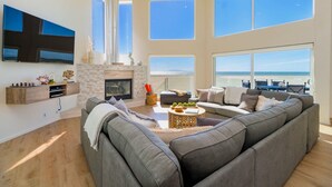 A spacious living room with a large gray sectional sofa, a fireplace, and a view of the beach.