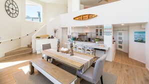 A spacious living area with a wooden dining table, a staircase, and a kitchen in the background.