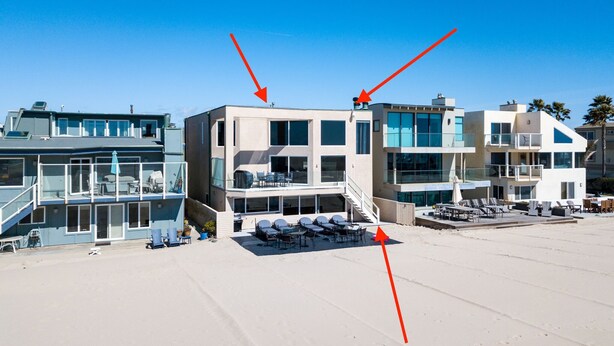A modern beachfront property with multiple levels, outdoor seating areas, and a clear view of the ocean.