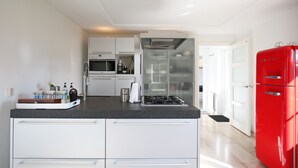 A modern kitchen with white cabinetry, a black countertop, a red refrigerator, and a glass door leading to a dining area. - Casa Grande - An amazing house 1 km from Amsterdam (Landsmeer)