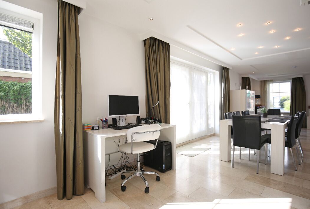 A modern office space with a desk, computer, and office chair. There is a dining area with a table and chairs.
