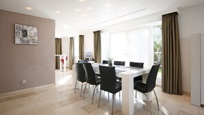 A modern dining area with a white table and black chairs, large windows with curtains, and recessed ceiling lighting. - Casa Grande - An amazing house 1 km from Amsterdam (Landsmeer)