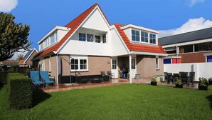 A two-story house with a red-tiled roof, a covered patio area with outdoor furniture, and a well-maintained lawn. - Casa Grande - An amazing house 1 km from Amsterdam (Landsmeer)