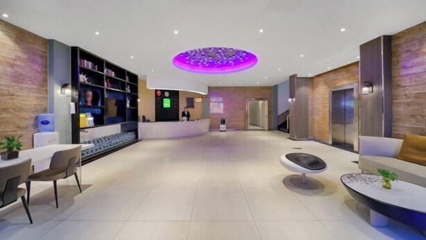 A modern lobby with a reception desk, seating area, and a circular ceiling light. - Snail House Hotel (Zhengzhou)