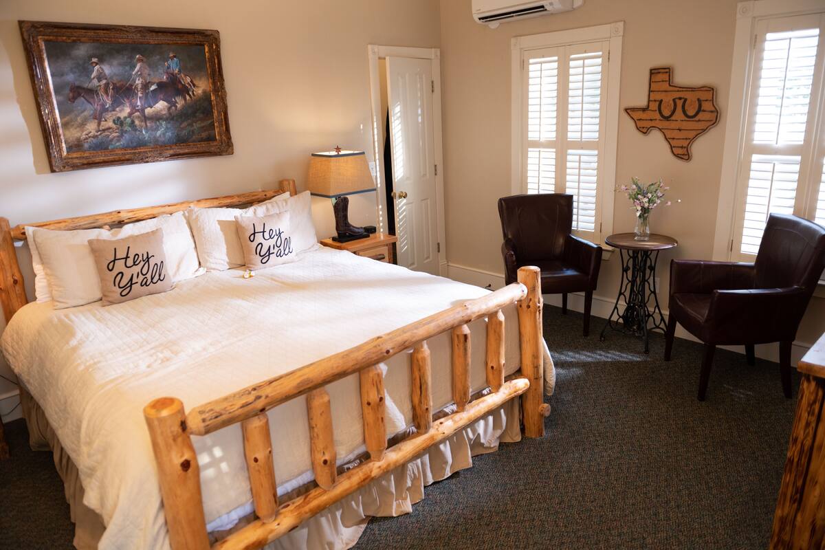 Un dormitorio con una cama de madera, una mesita de noche, una lámpara, una silla y una mesa con un jarrón de flores.
