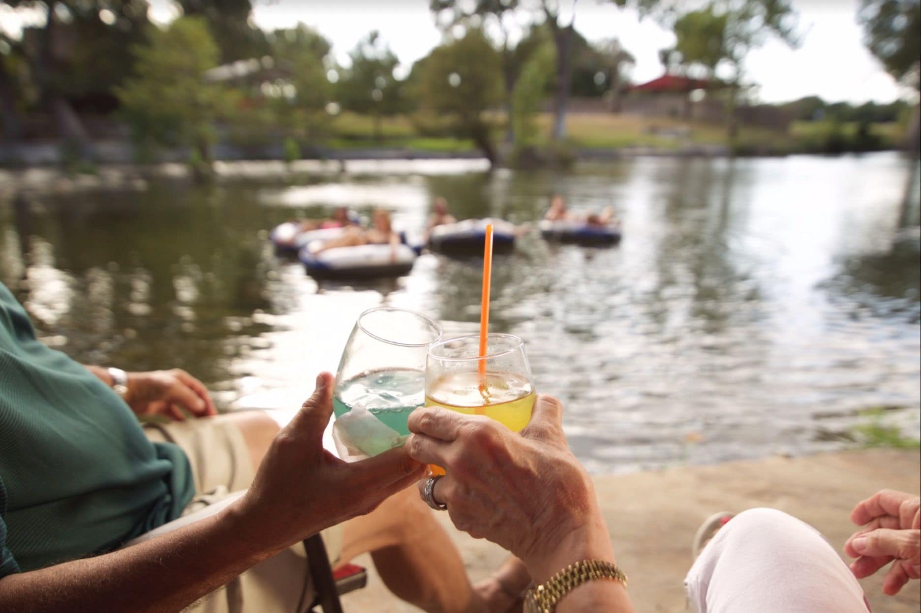 A group of people sitting by a lake, holding drinks.