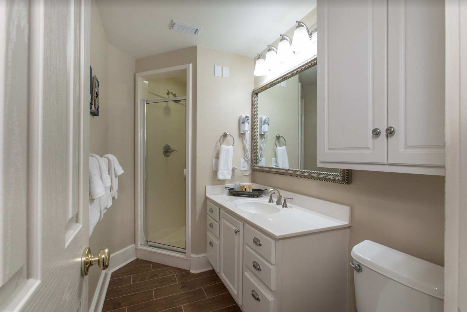 A bathroom with a glass shower door, a white sink, a large mirror, and a toilet.