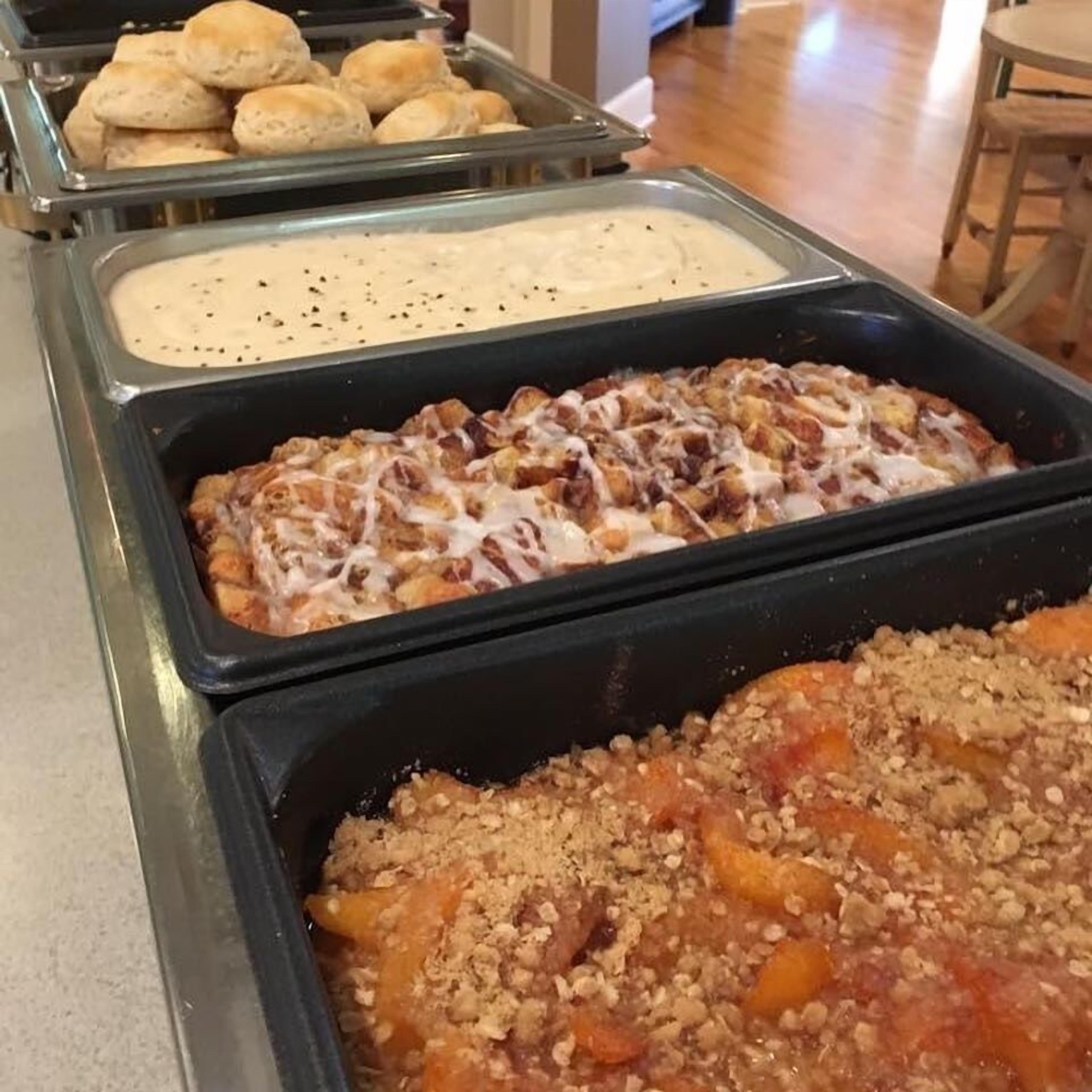 A buffet with various food items including bread rolls, a casserole dish, and a dessert with a crumbly topping.