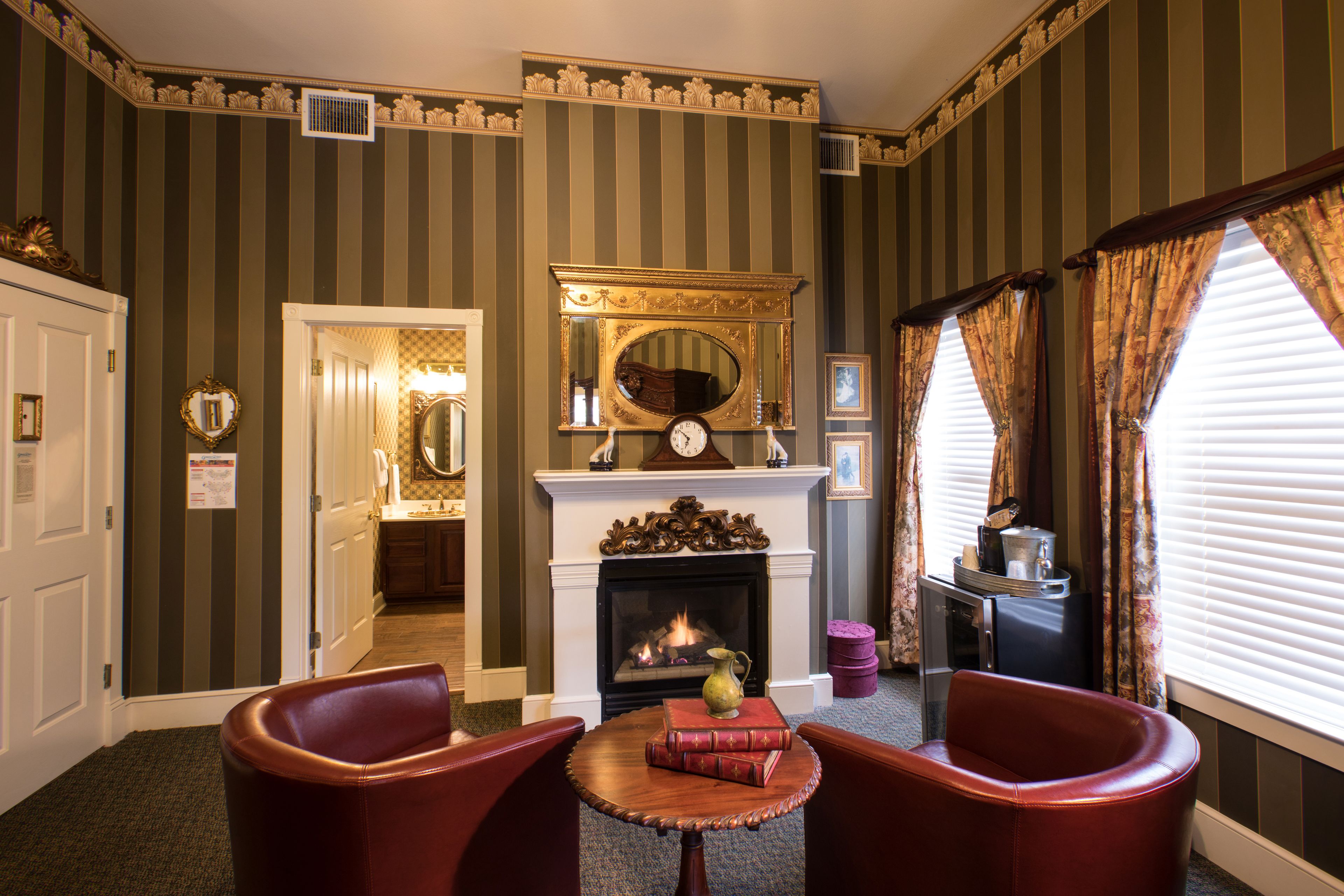 A room with striped wallpaper, a fireplace, a clock, and two leather chairs.