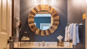 Un baño con un espejo redondo, dos lámparas, un perchero para toallas y un armario de madera.