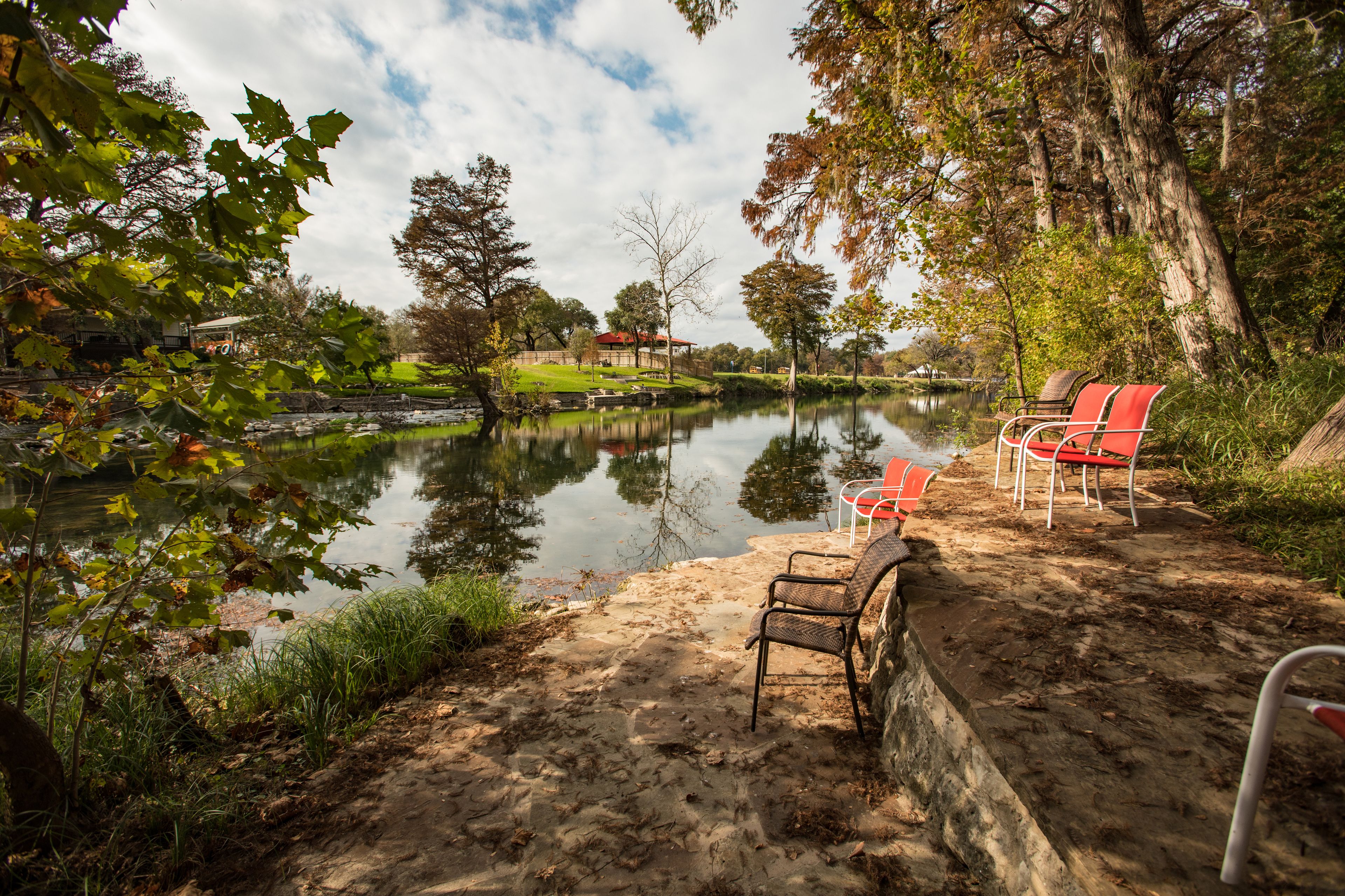 Un entorno tranquilo junto al lago, con una zona de arena, un banco y una silla cerca de la orilla.