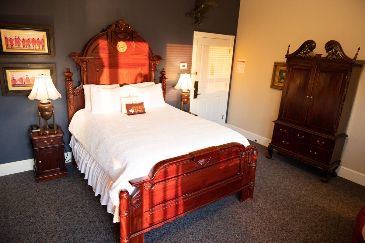 Un dormitorio con una cama de madera, dos mesitas de noche con lámparas, un armario y cuadros enmarcados en la pared.