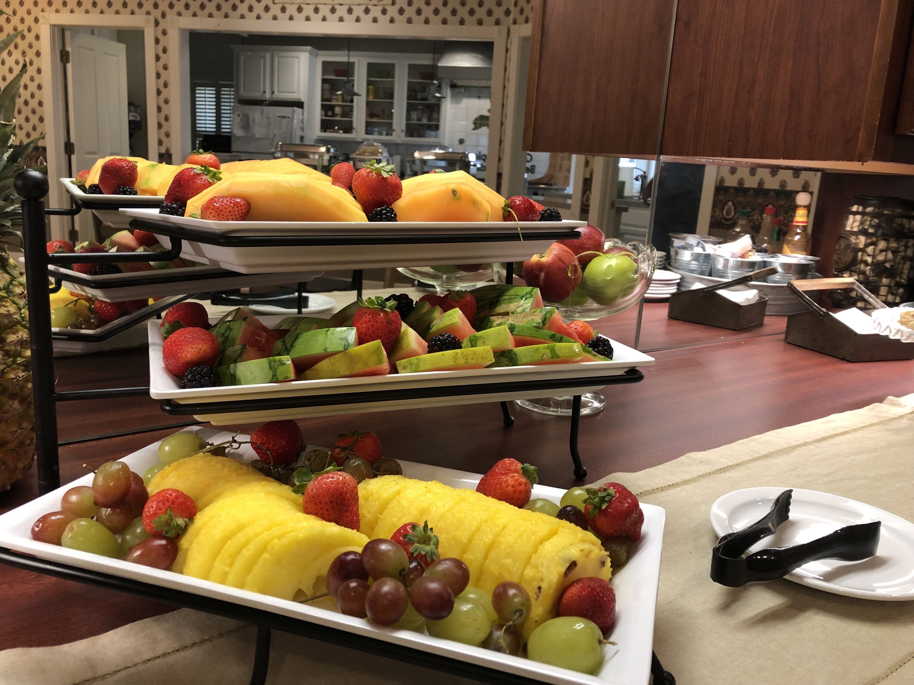 Un bufé con múltiples bandejas de frutas y verduras variadas.