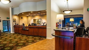 A hotel lobby with a reception desk, a large mirror, and a patterned carpet.