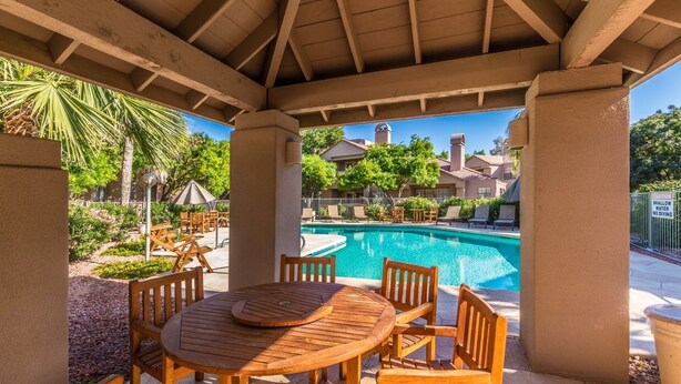 A covered outdoor area with a pool, wooden furniture, and a view of residential buildings. - LUXURY 2br/2baRemodel in the HEART of Scottsdale! HEATED POOL, GYM, TENNIS COURT (Scottsdale)