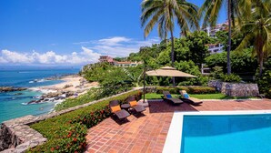 Un espace piscine avec des chaises longues et une vue sur la plage et l’océan.