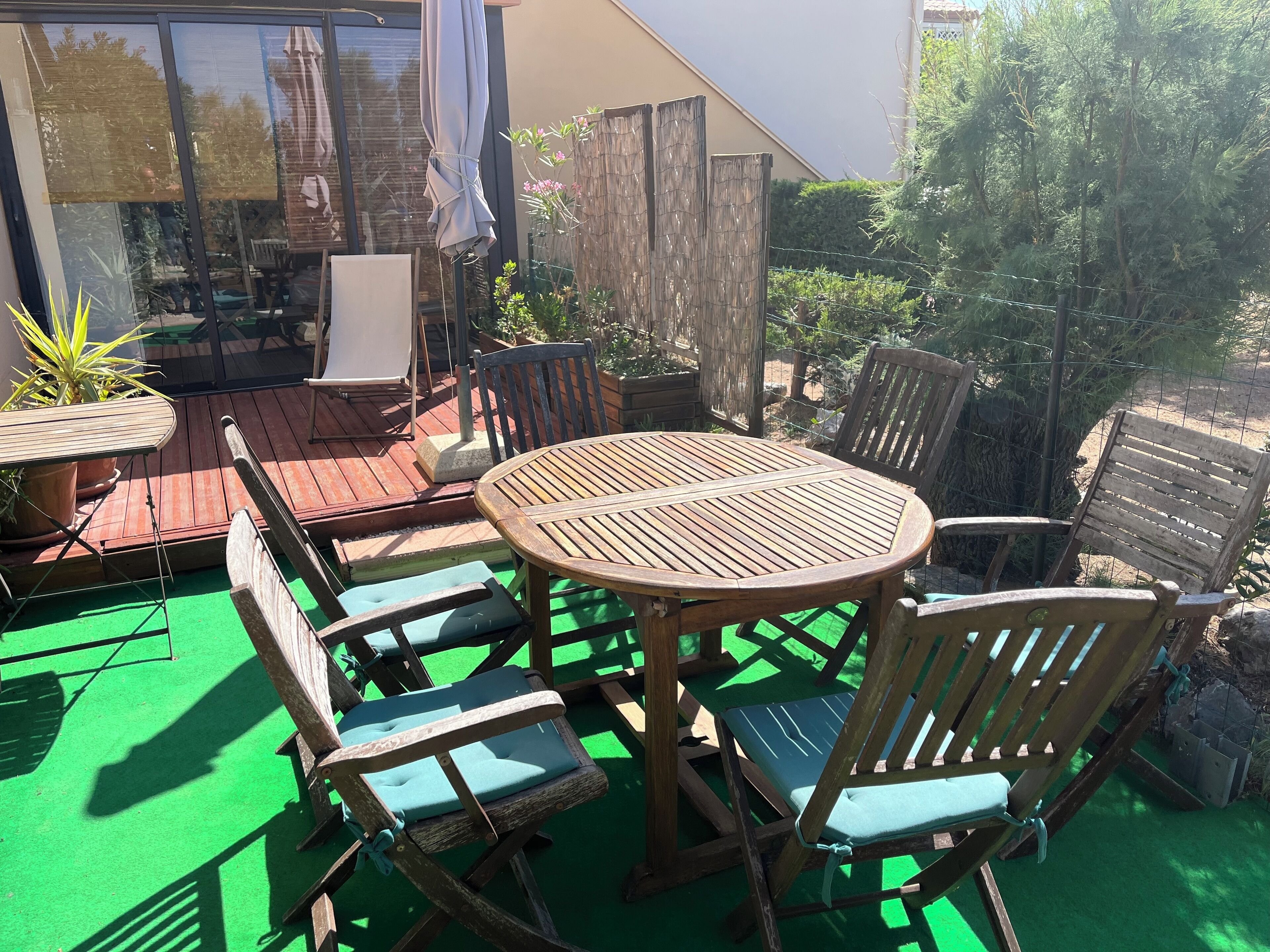Une terrasse en bois avec une table ronde et des chaises, entourée de plantes en pot et d’une clôture en bois.