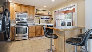 A kitchen with wooden cabinets, stainless steel appliances, a bar area with stools, and a 'God Bless Our Home' sign.