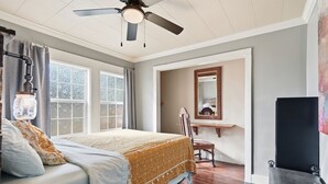 A bedroom with a bed, a chair, a vanity with a mirror, and a ceiling fan.