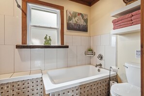 Et badeværelse med badekar, toilet og et vindue med en dekorativ hylde.