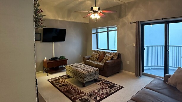 A spacious living room with a ceiling fan, a sofa, an ottoman, a TV, and a large window with a view. - 2nd Floor 'Sky Rise Vista' - Pool Access! (Sugar Mountain)