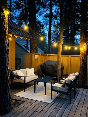 A deck with outdoor furniture, string lights, and a covered grill area.