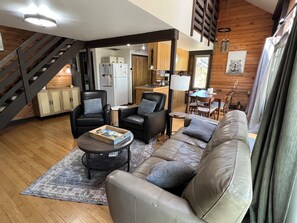 A cozy living area with a sofa, chairs, a coffee table, and a staircase. - Stylish Sunriver Cabin 2 Bed 2 bath + Loft, 6 SHARC Passes, Pet Friendly! (Bend)