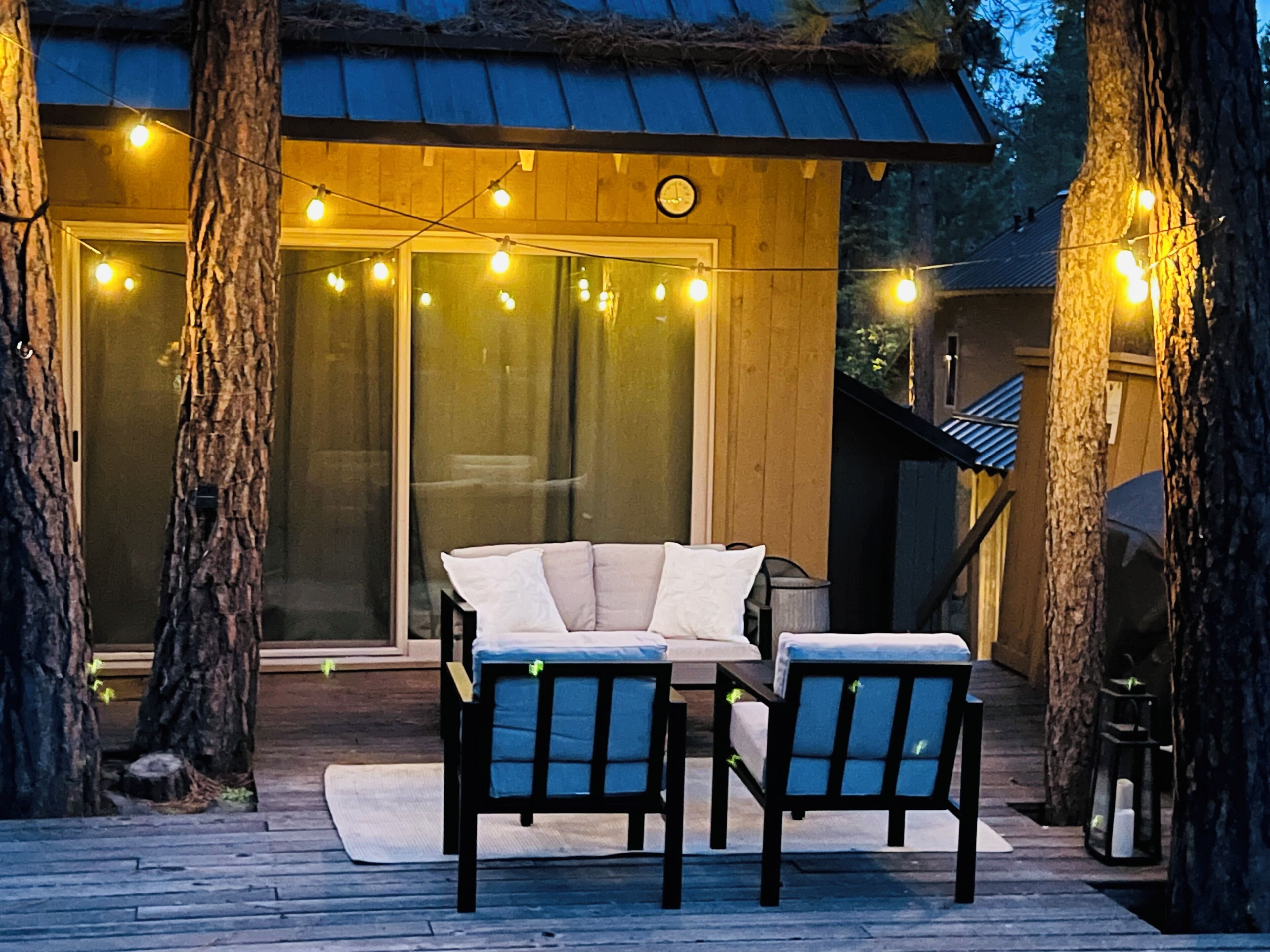 An outdoor deck with a sofa and chairs, string lights, and a wooden building with large windows.