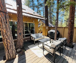 A wooden deck with a sofa and table, surrounded by trees. - Stylish Sunriver Cabin 2 Bed 2 bath + Loft, 6 SHARC Passes, Pet Friendly! (Bend)