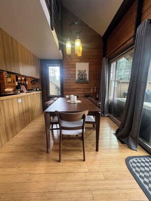 A dining area with a wooden table and chairs, a kitchen area with wooden cabinets, and a large window with curtains.