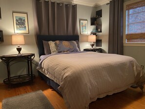 A bedroom with a bed, two bedside tables, a lamp, a rug, and a window with curtains.