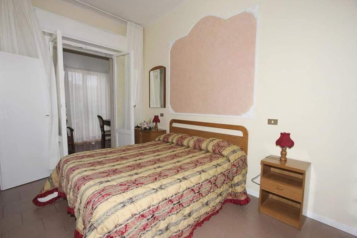 Een slaapkamer met een bed, een nachtkastje, een spiegel en een deur naar een andere kamer.