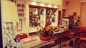 Angolo bar con bancone, scaffali pieni di bottiglie, macchina per il caffè e un'esposizione di fiori.