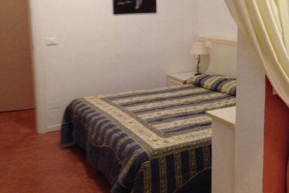 Een slaapkamer met een bed, nachtkastje, lamp en een poster aan de muur.