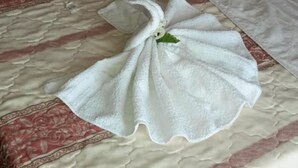 Una camera d'hotel con un letto, una coperta con motivi rossi e beige e due asciugamani disposti a forma di cigno.