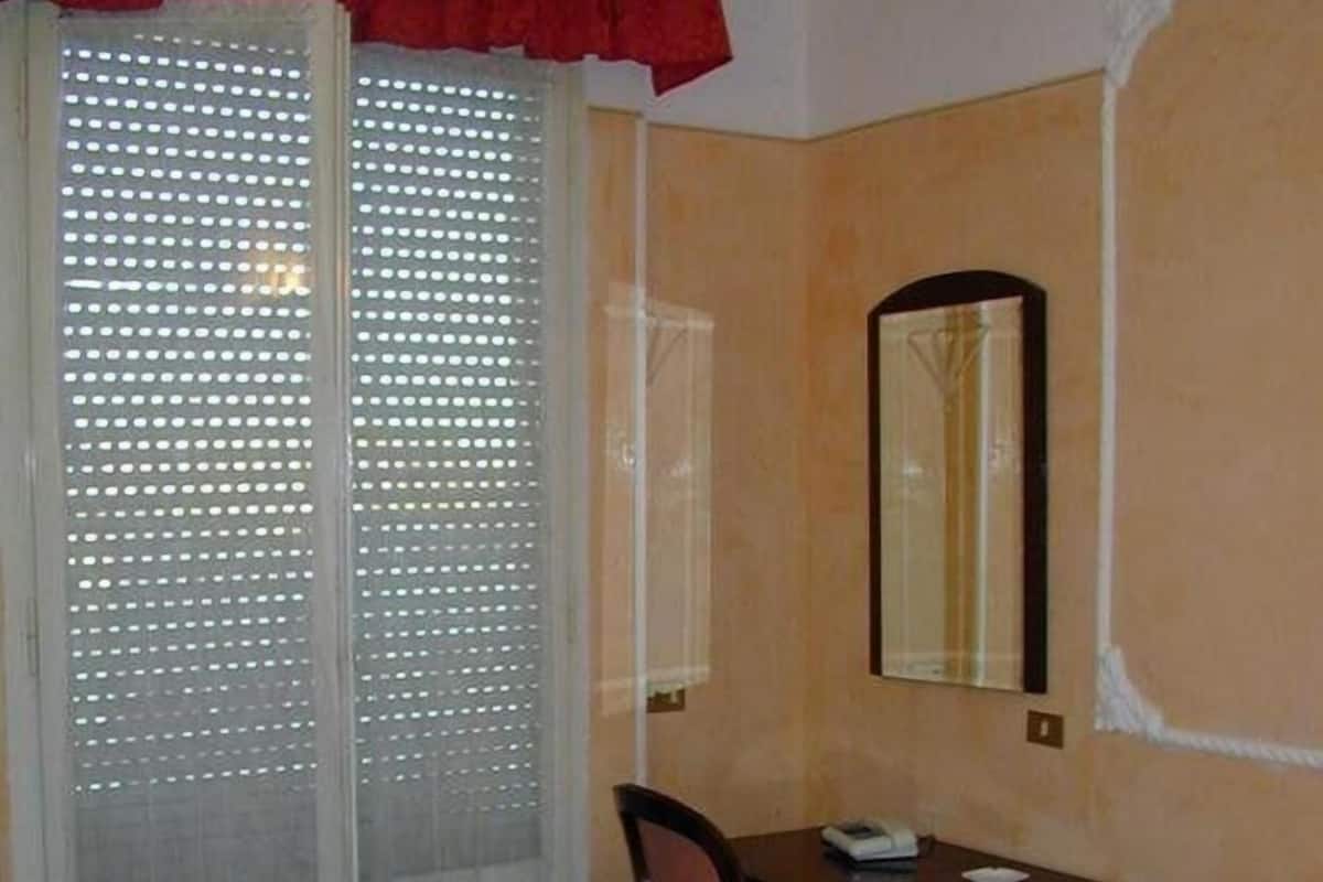 Hotelkamer met een bed, een bureau met stoel, een spiegel en een schuifdeur met een matglazen paneel.
