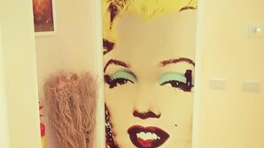Un corridoio con una porta decorata da un murale in stile pop art, un estintore e un cartello con un numero sopra la porta.