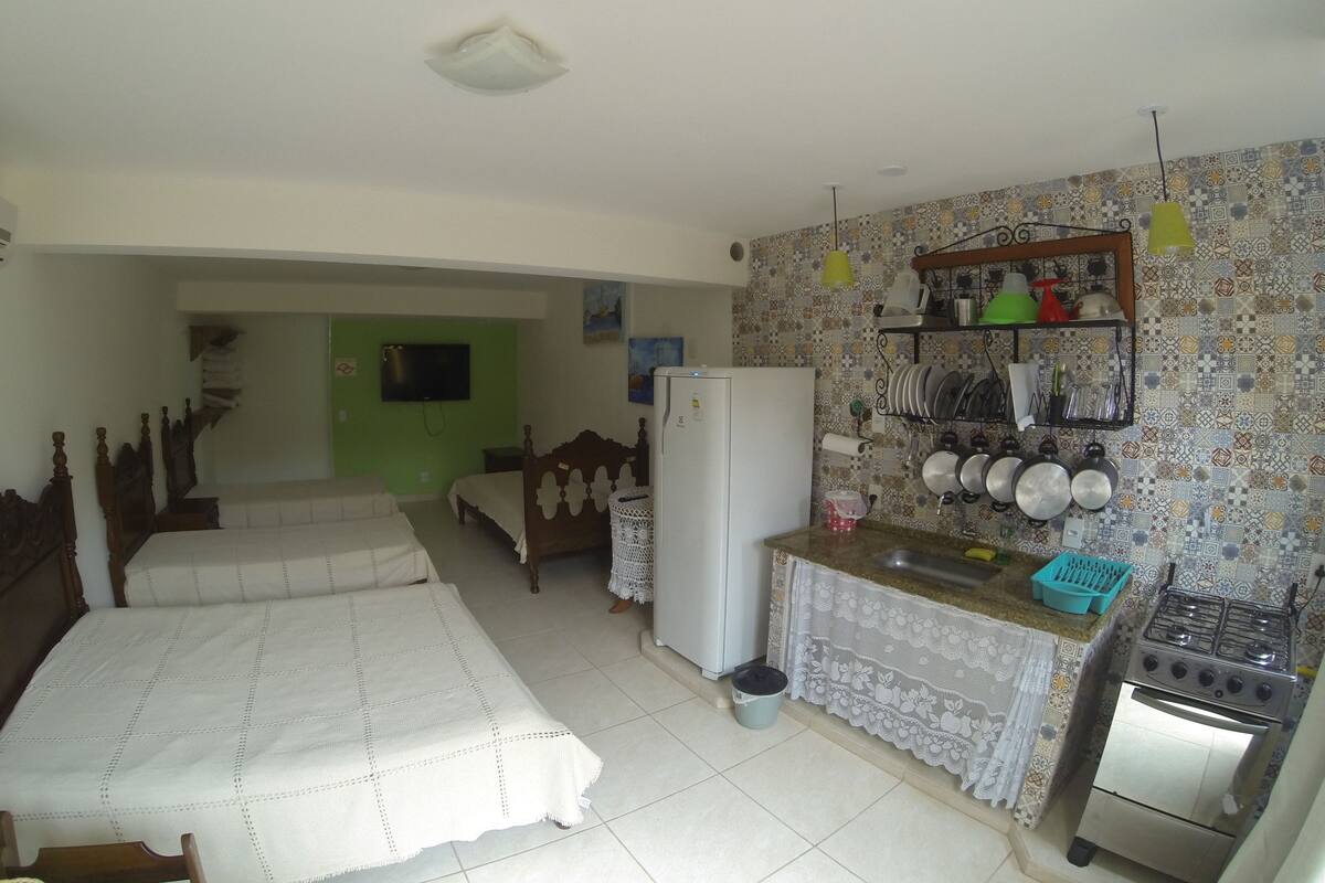 Een compacte keuken met een fornuis, wastafel en een kleine koelkast. Er is een eethoek met een tafel en stoelen, en een slaapkamer met een bed en een kledingkast.