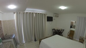 Een hotelkamer met een bed, een bureau met telefoon, een stoel, een klein tafeltje en een televisie aan de muur.