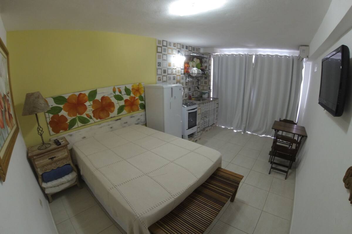 Een compacte kamer met een bed, een klein kitchenette, een televisie en een raam met gordijnen.