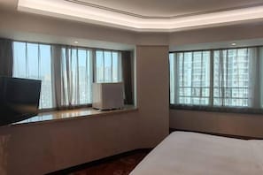 A hotel room with a bed, a flat-screen TV, a heater, and large windows with curtains. - Bonway International Hotel (Shiyan)