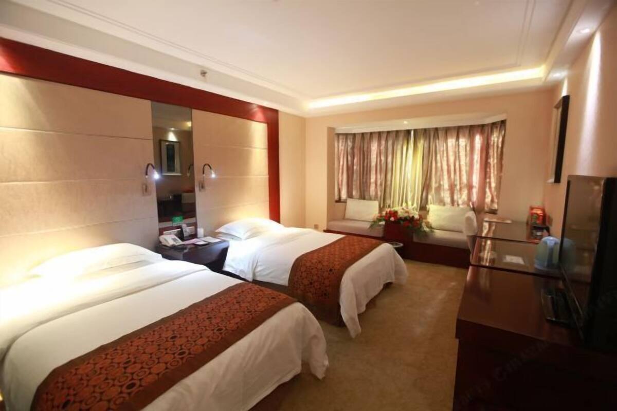 Ein Hotelzimmer mit zwei Betten, einer Couch, einem Fernseher und einem Fenster mit Vorhängen.