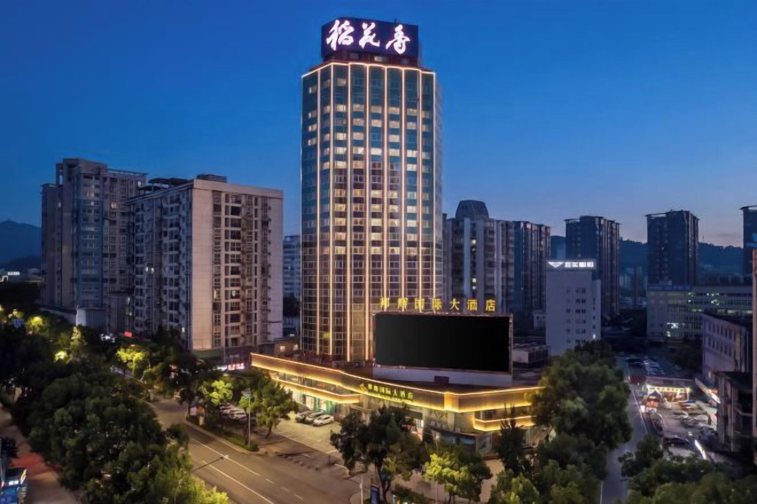 A high-rise hotel with a prominent sign, surrounded by other buildings and a parking area.