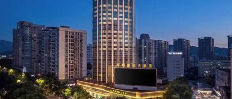 A high-rise hotel with a prominent sign, surrounded by other buildings and a parking area.