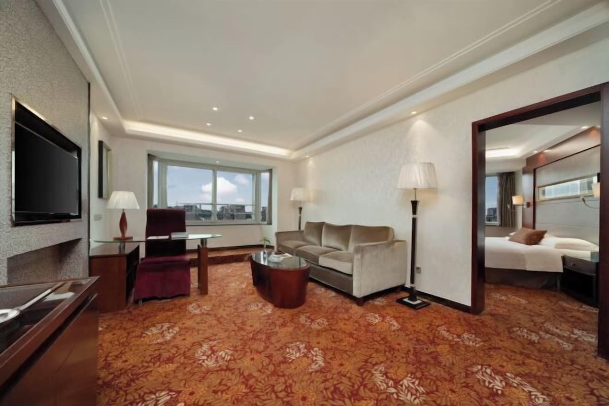 A hotel room with a flat-screen TV, a sofa, a coffee table, a lamp, and a large mirror.