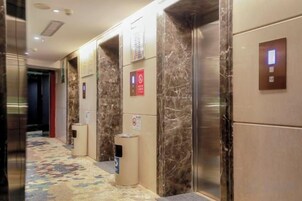 Un pasillo de hotel con paredes de mármol, ascensores y suelo alfombrado.