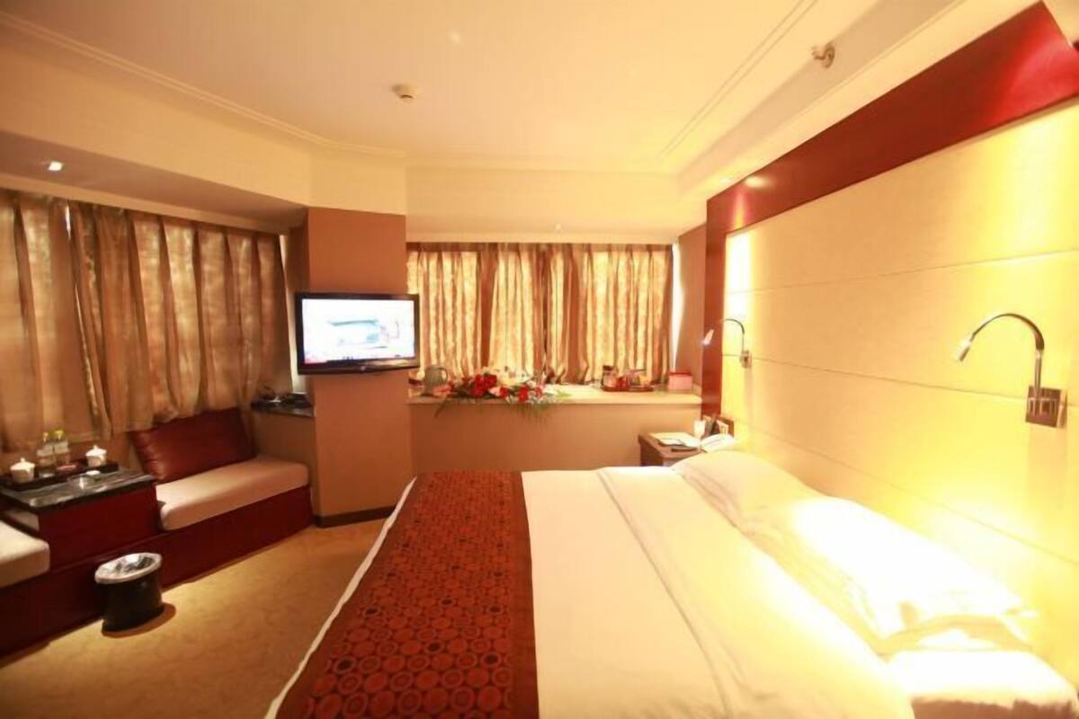 Ein Hotelzimmer mit Bett, Sofa, Fernseher, Schreibtisch und einem Fenster mit Vorhängen.
