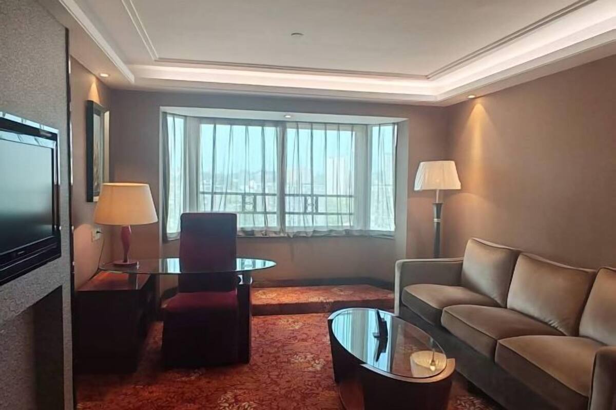 Ein Hotelzimmer mit großem Fenster, einer Couch, einem Sessel, einem Fernseher und einer Lampe.